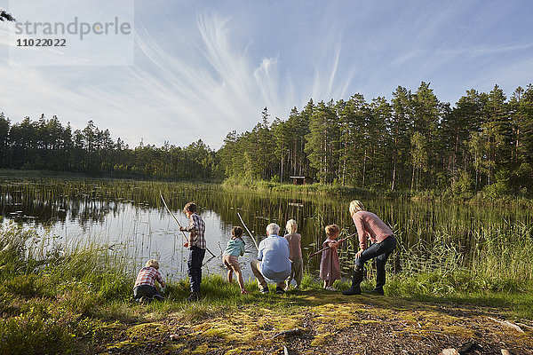 Großeltern und Enkelkinder beim Angeln am sonnigen Seeufer im Wald