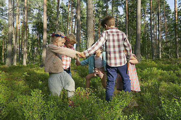 Jungen und Mädchen halten ihre Hände im Kreis zwischen Bäumen im Wald.