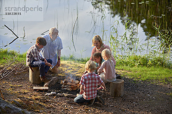 Großeltern und Enkelkinder beim Lagerfeuer am Seeufer