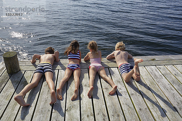 Jungen und Mädchen  die auf dem Dock liegen und auf den See blicken.