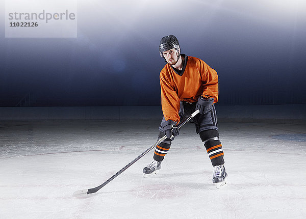 Portrait selbstbewusster Hockeyspieler in oranger Uniform auf Eis