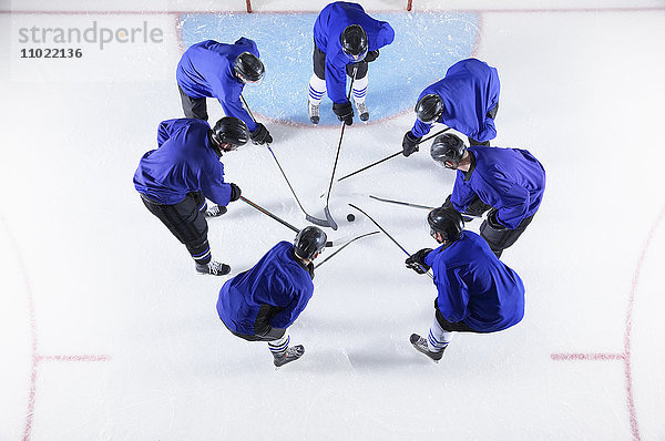 Hockeyspieler in blauen Uniformen kauern um den Puck auf dem Eis.