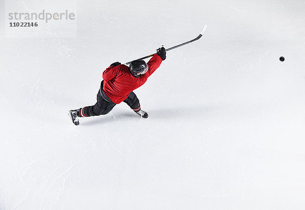 Hockeyspieler in roter Uniform schießt Puck auf Eis