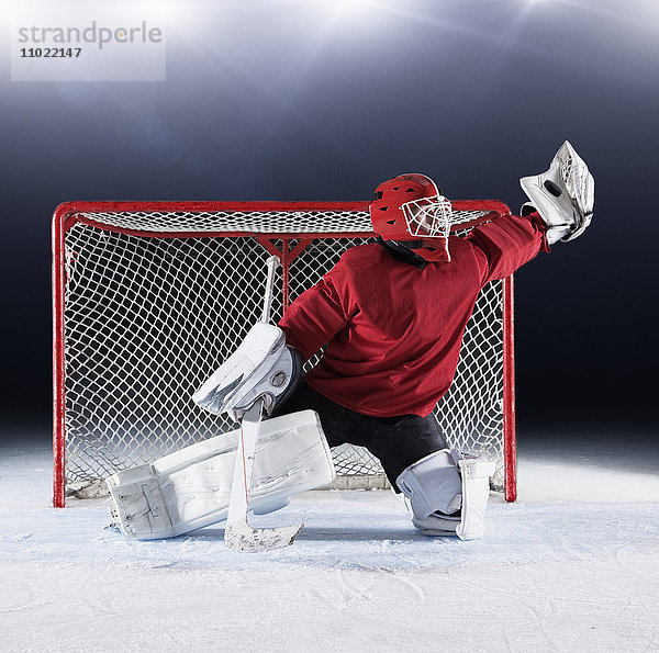 Hockeytorwart in roter Uniform mit Handschuhen am Tornetz