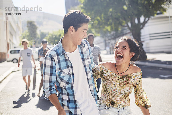 Lachendes Teenager-Paar auf der sonnigen Stadtstraße