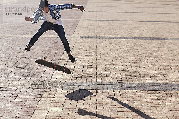 Teenager Junge flippt Skateboard auf sonnigem Kopfsteinpflaster