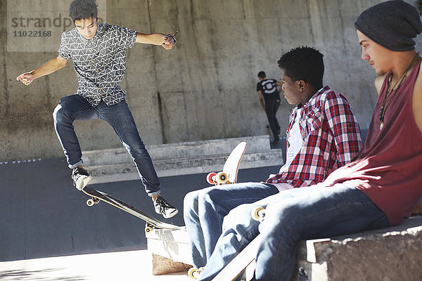 Freunde sehen Teenager beim Stunt im Skatepark zu.