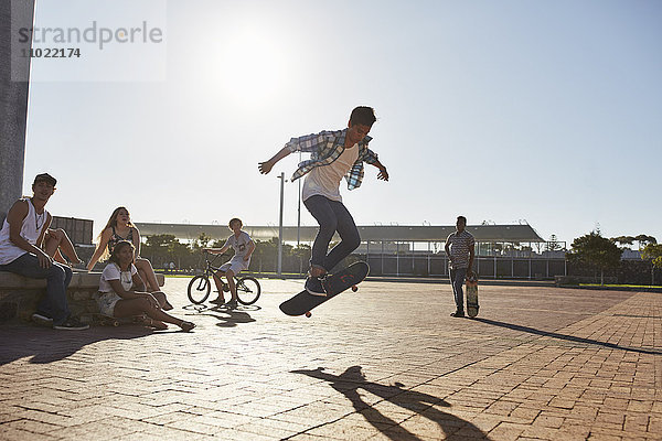 Freunde sehen dem Teenager beim Skateboardfahren im sonnigen Skatepark zu.