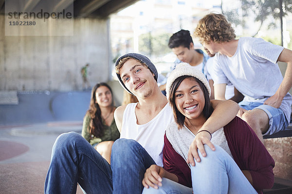 Portrait lächelndes Teenager-Pärchen mit Freunden im Skatepark