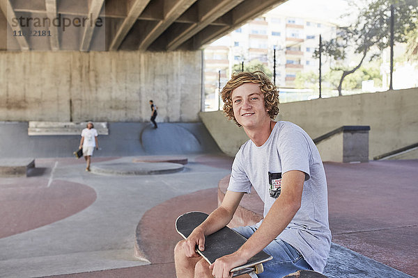 Portrait lächelnder Teenager mit Skateboard im Skatepark