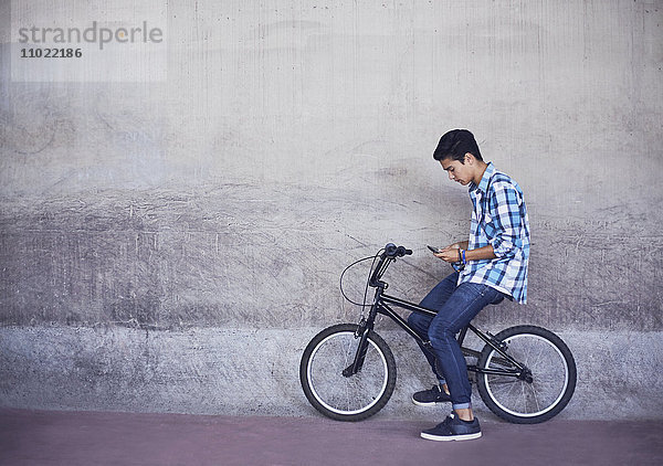 Teenage boy texting auf BMX Fahrrad an der Wand