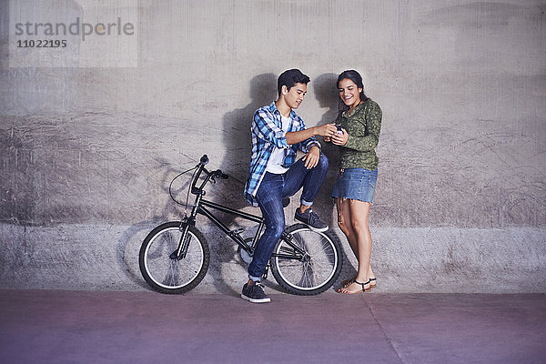 Teenager-Paar mit BMX-Fahrrad SMS an der Wand