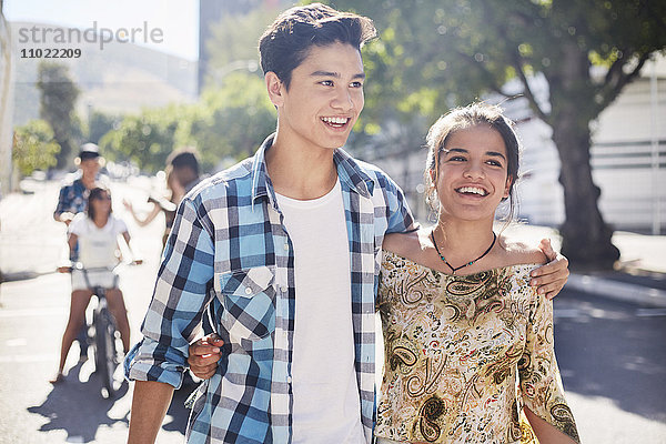 Lächelndes Teenager-Paar  das auf einer sonnigen  städtischen Straße spazieren geht.