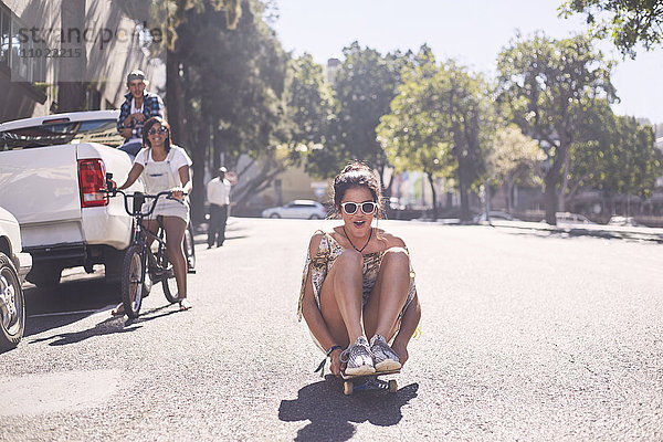 Teenager-Mädchen sitzt auf einem Skateboard auf einer sonnigen  städtischen Straße.