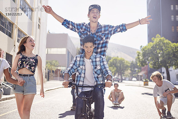 Teenager-Freunde beim BMX-Radfahren und Skateboarden auf der sonnigen Stadtstraße