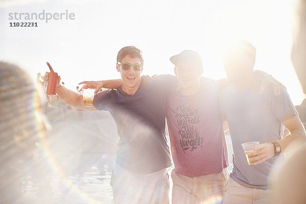 Portrait junge Männer beim Biertrinken auf der sonnigen Poolparty