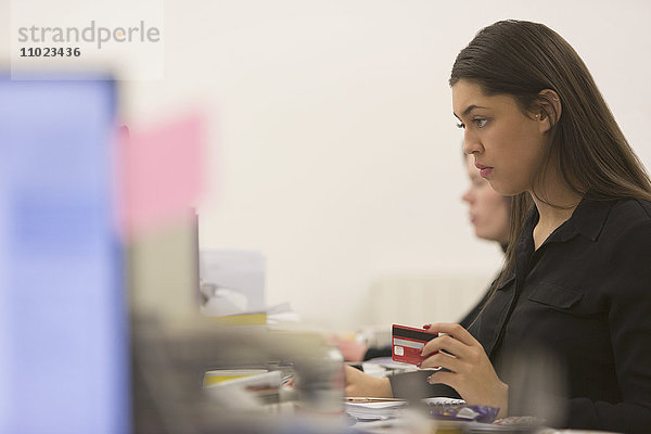 Konzentrierte Geschäftsfrau mit Kreditkarte am Computer im Büro