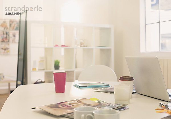 Laptop  Kaffeetassen und Modezeitschriften auf dem Tisch im Büro