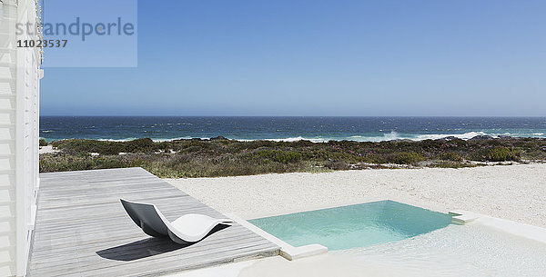 Pool und moderner Liegestuhl mit Blick auf das Meer unter sonnigem  blauem Himmel