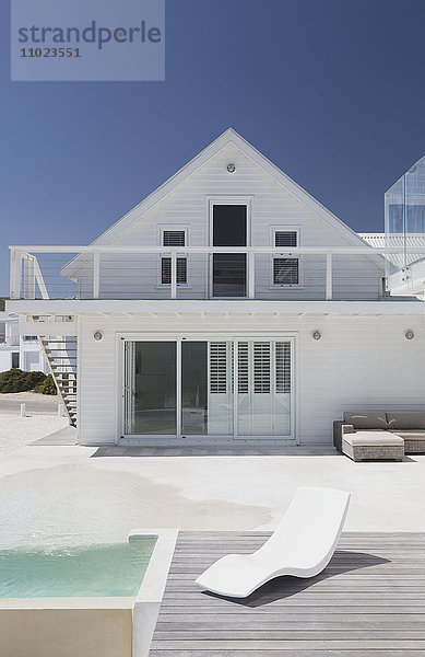 Weißes Haus mit Schwimmbad und modernem Sessel unter sonnigem blauem Himmel