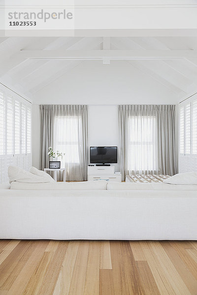 Weißes Wohnzimmer mit gewölbter Holzbalkendecke in einem Musterhaus