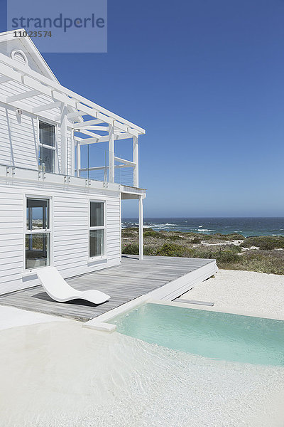 Weißes Strandhaus und Swimmingpool mit Blick auf das Meer unter sonnigem blauem Himmel