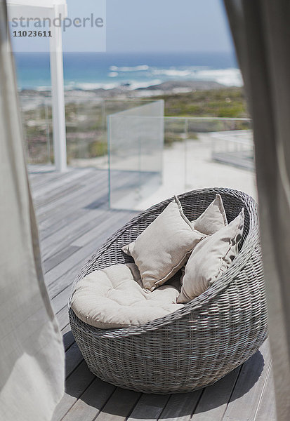 Korbstuhl mit Kissen auf der sonnigen Terrasse des Strandhauses mit Meerblick