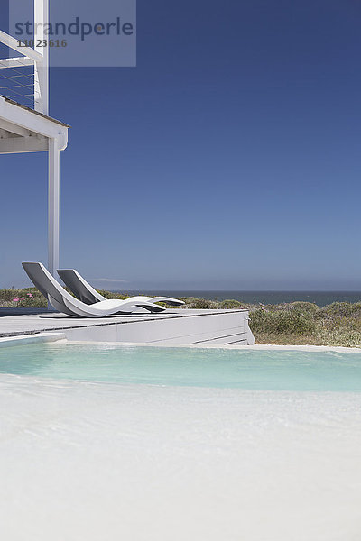 Moderne Liegestühle am Pool mit Blick auf das Meer unter sonnigem blauem Himmel