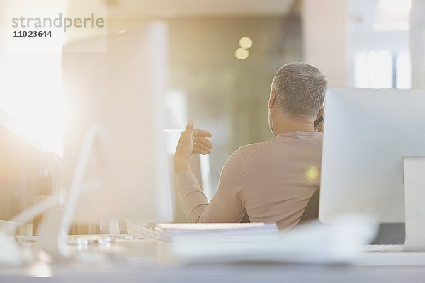 Geschäftsmann gestikuliert am Schreibtisch in einem sonnigen Büro