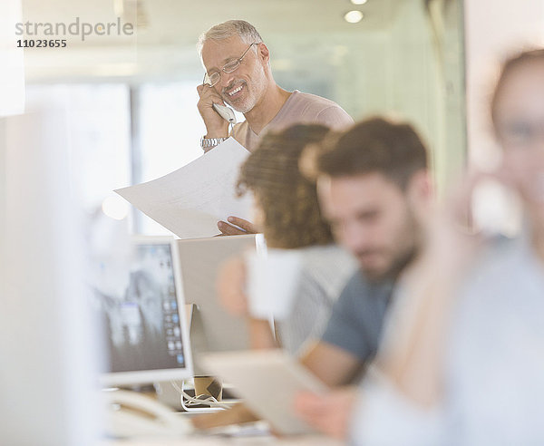 Architekt mit Bauplänen  der in einem Büro telefoniert