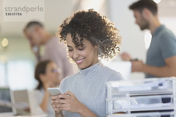 Lächelnde Geschäftsfrau  die mit ihrem Handy im Büro SMS schreibt