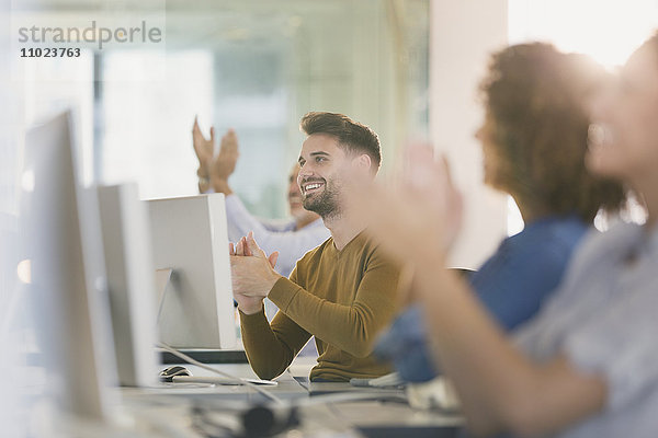 Geschäftsleute an Computern  die im Büro klatschen