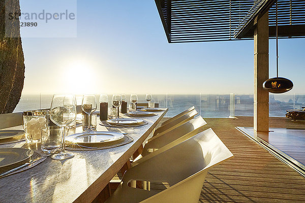 Die Sonne scheint über dem Meer hinter dem luxuriösen Esstisch auf der Terrasse mit Sitzgelegenheiten