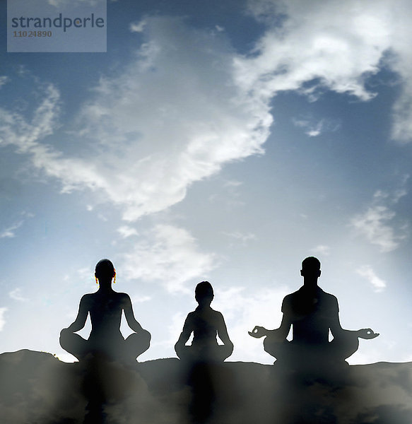 Silhouette einer meditierenden Familie gegen blauen Himmel im Lotussitz