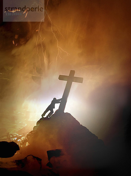 Mann schiebt ein religiöses Kreuz über brennende Hölle