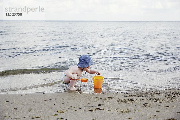 Junge spielt am Strand mit Eimer und Schaufel
