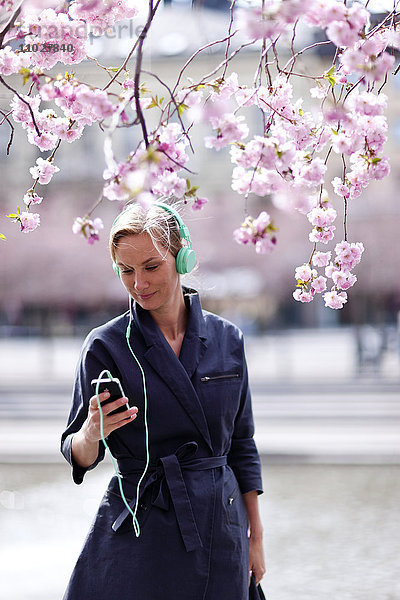 Junge Frau mit mp3-Player in der Nähe von Kirschblütenbäumen