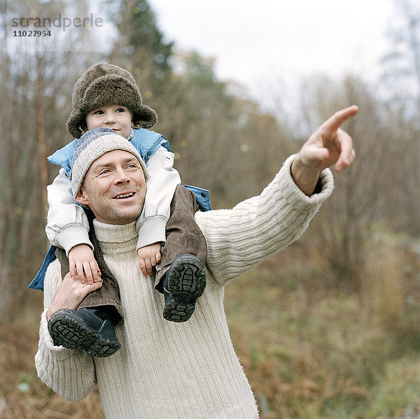 Ein Kind reitet an einem Herbsttag auf den Schultern seines Vaters.