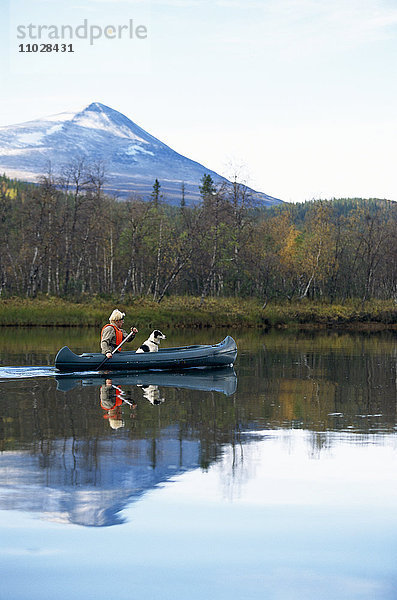 Eine Person paddelt mit einem Hund in einem Kanu auf ruhigem Wasser.