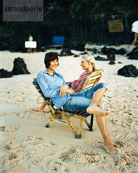 Ein Mann und eine Frau sitzen in Liegestühlen am Strand.