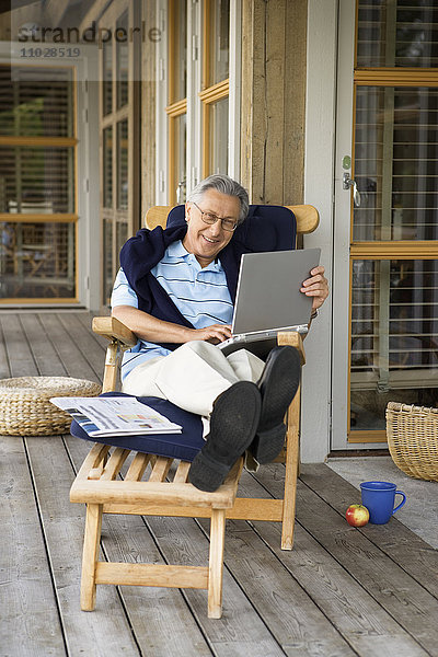 Ein Mann sitzt in einem Liegestuhl mit einem Laptop.