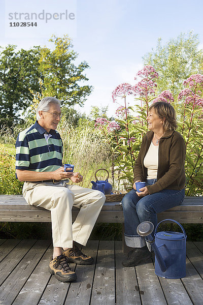 Ein Mann und eine Frau trinken Tee auf einer Bank im Freien.