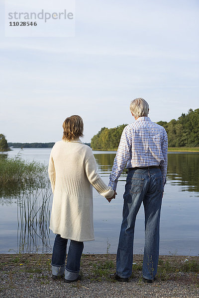 Ein Mann und eine Frau halten sich an einem See die Hand.