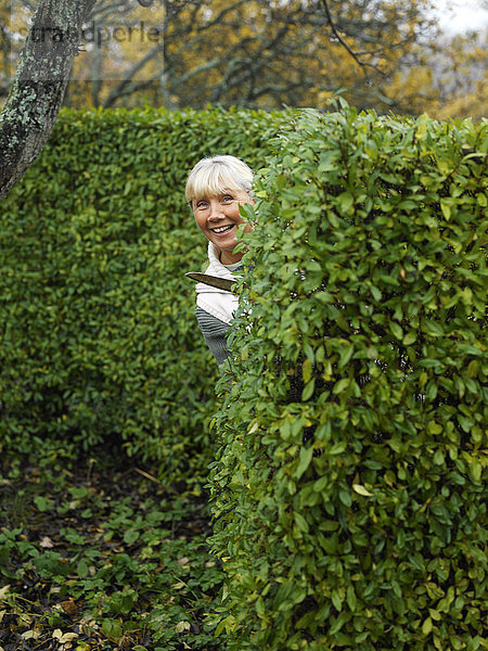 Eine lächelnde Frau beim Schneiden einer Hecke.