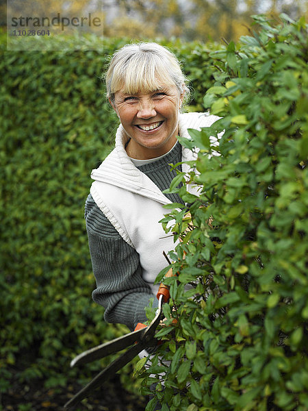 Eine lächelnde Frau beim Schneiden einer Hecke.