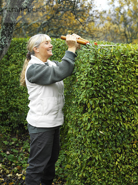 Eine Frau schneidet eine Hecke.