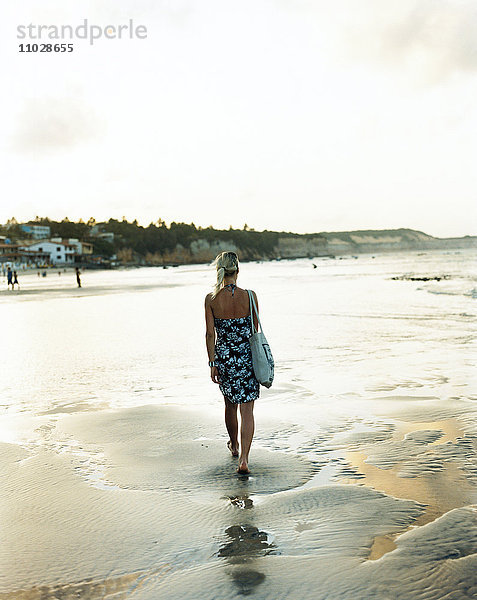 Frau läuft barfuß am Strand.