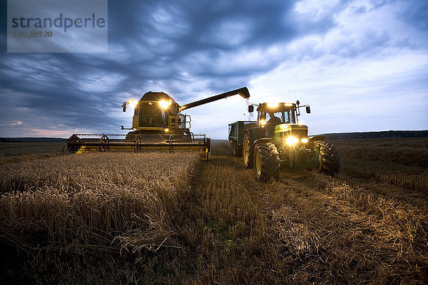 Mähdrescher und Traktor auf einem Feld in der Abenddämmerung