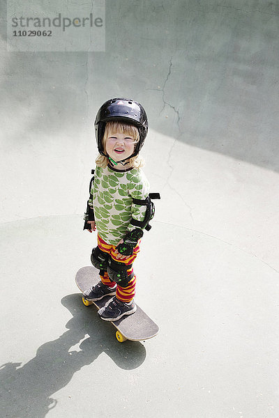 Porträt eines Jungen  der auf einem Skateboard steht und in die Kamera schaut