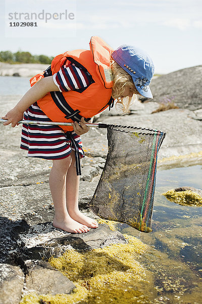 Mädchen steht am Rande des Wassers und hält ein Schmetterlingsfangnetz